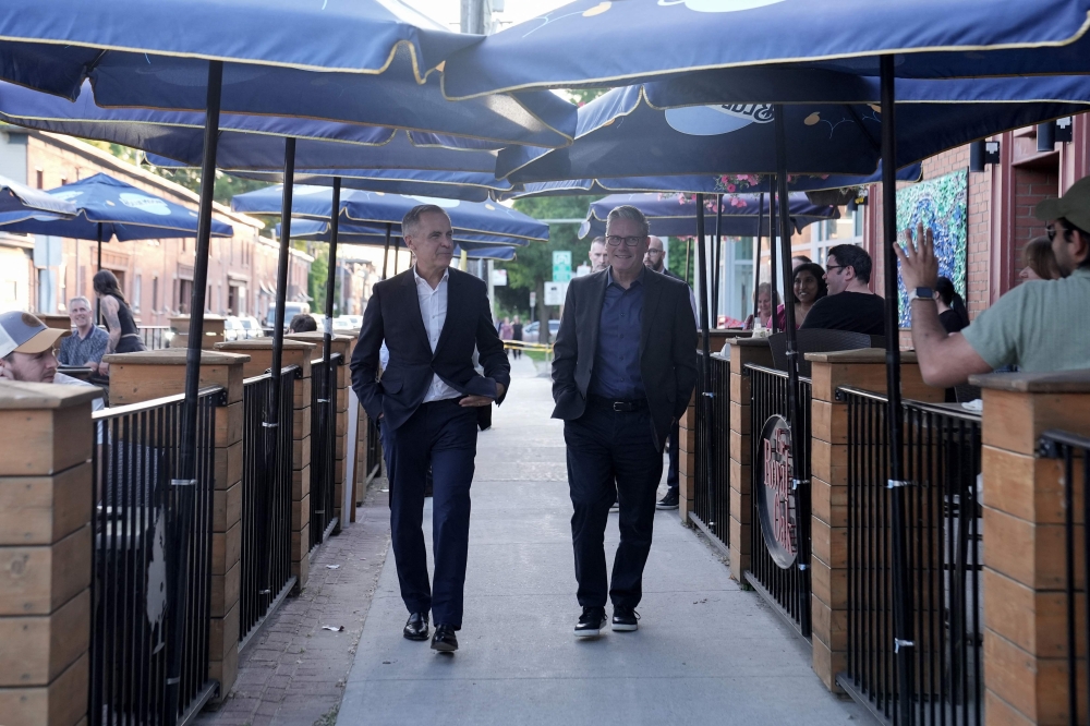 Onlookers wave as British Prime Minister Keir Starmer (R) and Canadian Prime Minister Mark Carney arrive at the Royal Oak pub in Ottawa, Canada, on June 14, 2025 to watch the Stanley Cup Final ice hockey match on television, ahead of the G7 leaders' summit. (Photo by Stefan Rousseau / POOL / AFP)