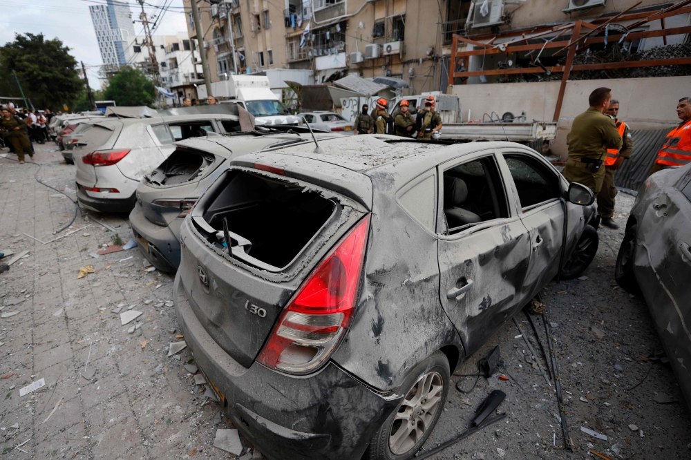 Rescuers work near a damaged building and damaged cars following a strike by an Iranian missile in the Israeli city of Bnei Brak, east of Tel Aviv, on June 16, 2025. (Photo by Jalaa Marey / AFP)