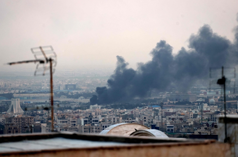 Smoke billows from an explosion near the Azadi Tower (L) in Tehran on June 16, 2025. (Photo by Atta Kenare / AFP)