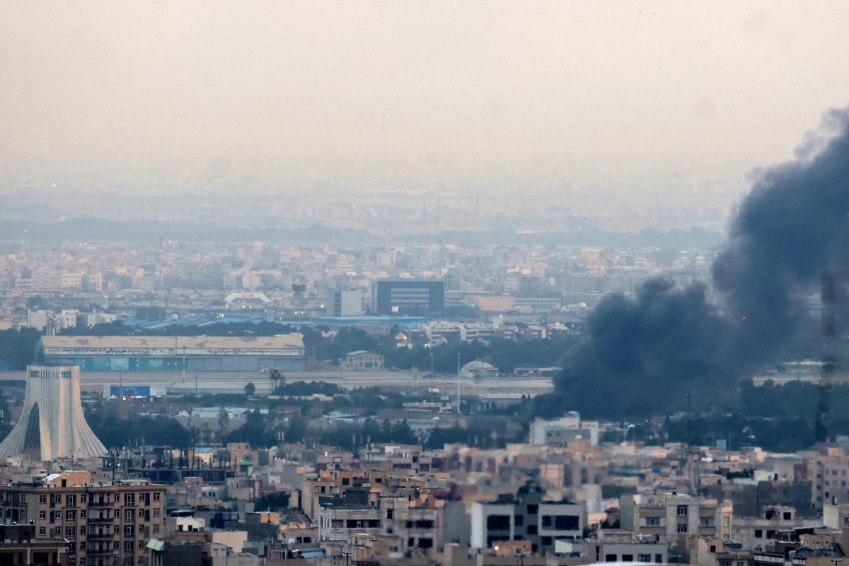 Smoke billows from a site near the Azadi Tower (L) in central Tehran, as fighting between Israel and Iran continues on June 16, 2025. Photo by ATTA KENARE / AFP.
