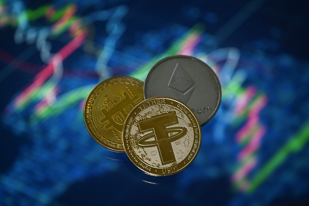 (Files) An illustration picture taken in London on May 8, 2022, shows gold plated souvenir cryptocurrency Tether (USDT), Bitcoin and Etherium coins arranged beside a screen displaying a trading chart. (Photo by Justin Tallis / AFP)
