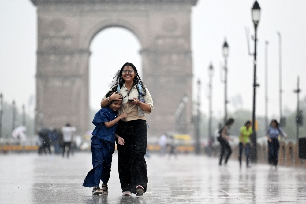 Girls walk along a road at the India Gate as it rains in New Delhi on June 17, 2025. (Photo by Arun Sankar / AFP)