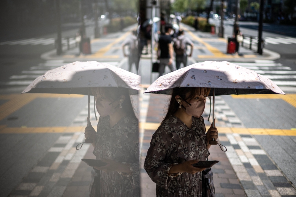A woman uses an umbrella to shield from the sun as she walks down a street at the Yurakucho district in Tokyo where temperatures have topped 34 degrees Celsius on June 18, 2025. (Photo by Philip Fong / AFP)