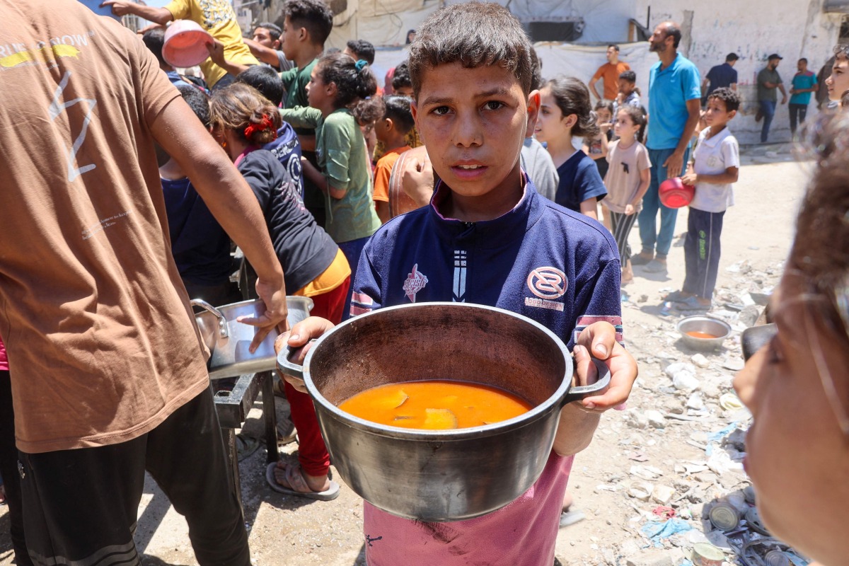 A Palestinian boy carries a pot with food collected at a charity kitchen providing hot meals in Rimal neighbourhood in Gaza City on June 18, 2025. Photo by Omar AL-QATTAA / AFP
