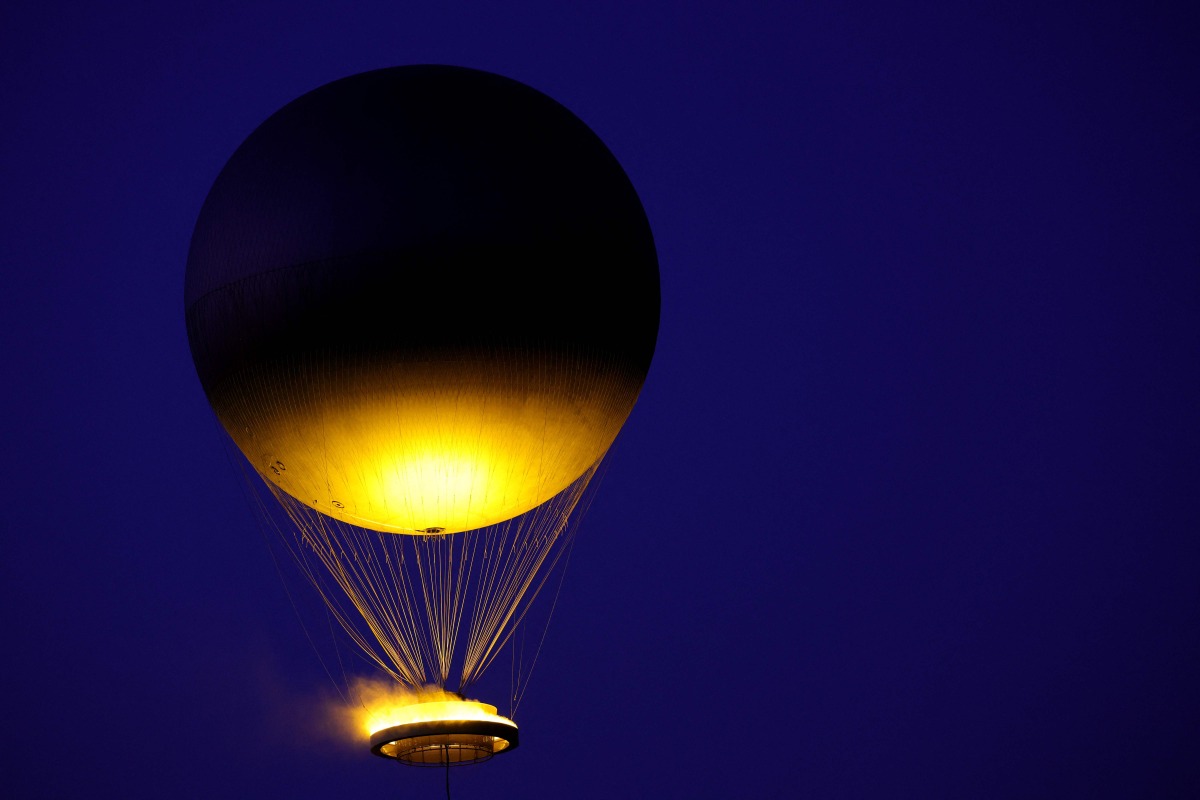The Paris 2024 Olympic cauldron tethered to a balloon, designed by French designer Mathieu Lehanneur, flies above the Tuileries garden at sunset during France's annual street music festival, the Fete de la Musique, in Paris on June 21, 2025. (Photo by ROMAIN PERROCHEAU / AFP)