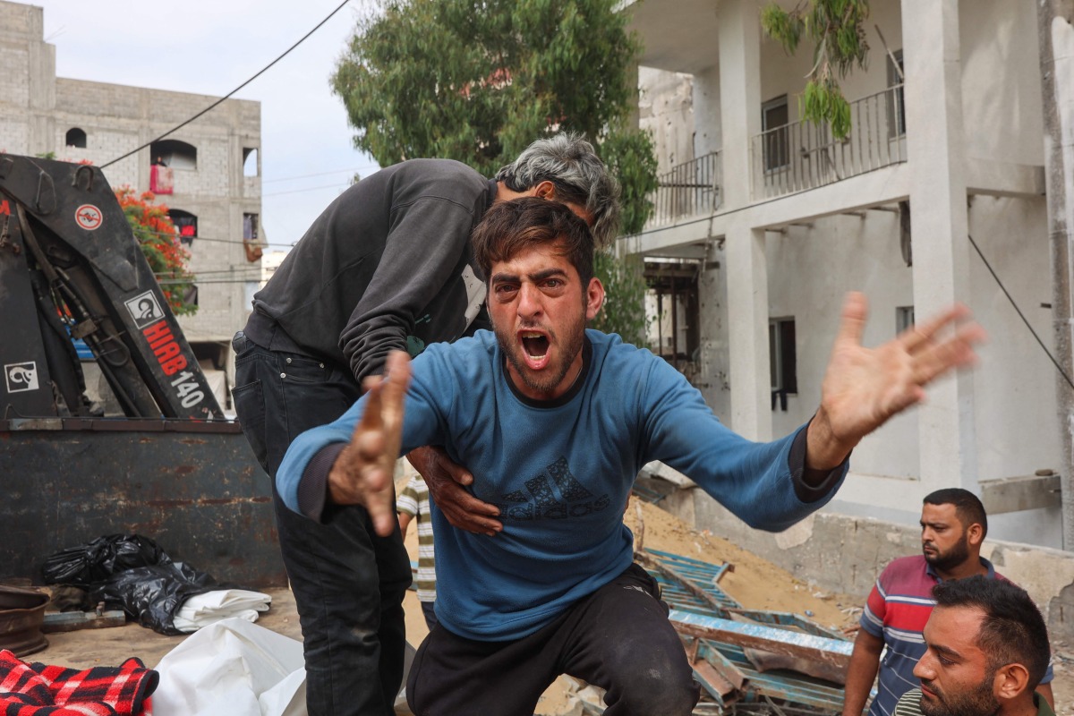 A Palestinian man mourns as others transport bodies of people killed in strikes on Jabalia a day earlier, at Al-Shifa hospital in Gaza City on June 23, 2025. (Photo by Omar AL-QATTAA / AFP)