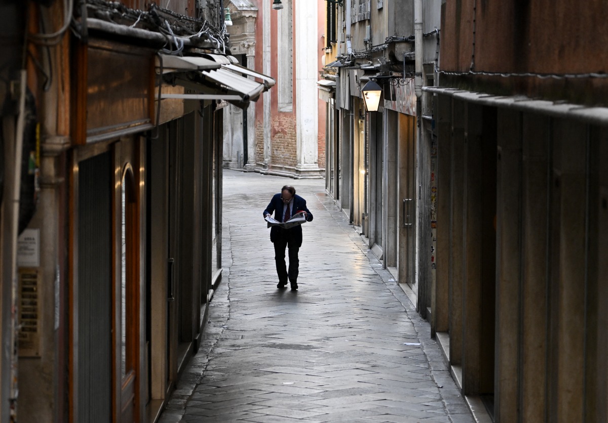 Photo used for representational purposes. A man reads a newspaper as he walks in a narrow street of venice, on June 24, 2025. Photo by Stefano RELLANDINI / AFP.