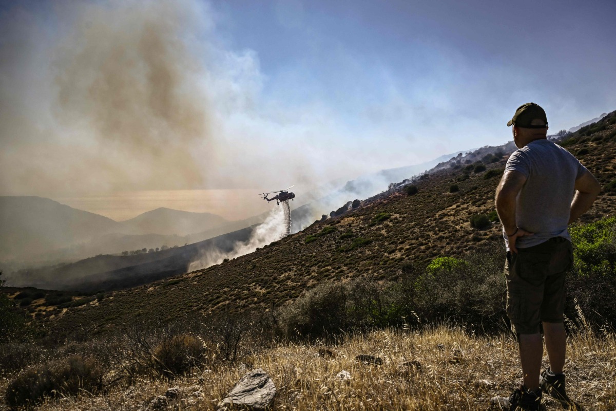 A resident watches a Sikorsky S-64 Skycrane dropping water on a forest fire, near Thymari, southeast of Athens, on June 26, 2025. Photo by Aris MESSINIS / AFP