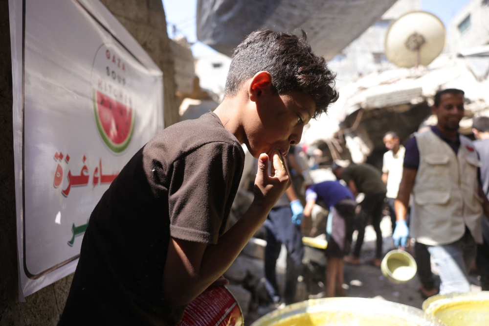 A Palestinian boy licks his fingers as he scrapes the pot for a portion of food at a food distribution point in Gaza City on June 27, 2025. (Photo by Bashar Taleb / AFP)