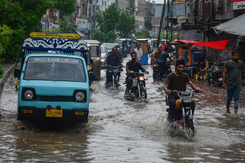 Commuters make their way through a flooded street following heavy rainfall in Hyderabad, in Sindh province on June 27, 2025. (Photo by Akram Shahid / AFP)
