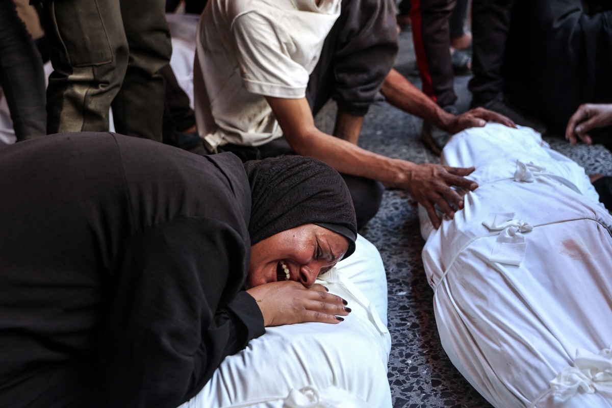 Palestinians mourn over the shrouded bodies of people killed during a reported Israeli strike on a humanitarian aid distribution warehouse in the Sabra neighbourhood in Gaza City, in the central Gaza Strip, on the grounds of Al-Ahli Arab hospital, also known as the Baptist hospital on June 30, 2025. (Photo by Omar AL-QATTAA / AFP)