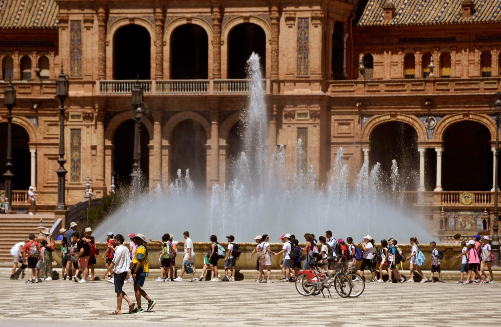 File: A group of schoolchildren on a excursion cool off walking along a fountain at the Plaza Espana square in Seville on April 26, 2023. (Photo by Cristina Quicler / AFP)