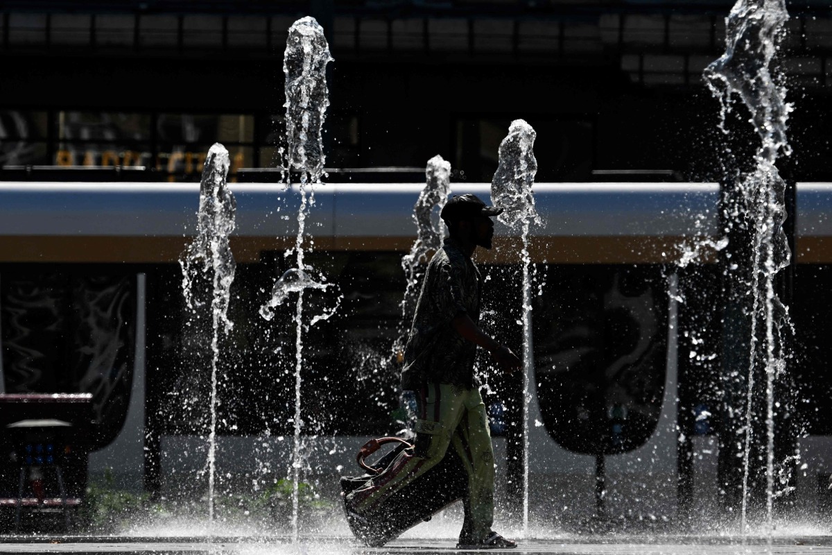 A man walks through the water jets of a public fountain as outside temperatures reach 37 degrees celsius in Brussels on July 1, 2025. Photo by Nicolas TUCAT / AFP
