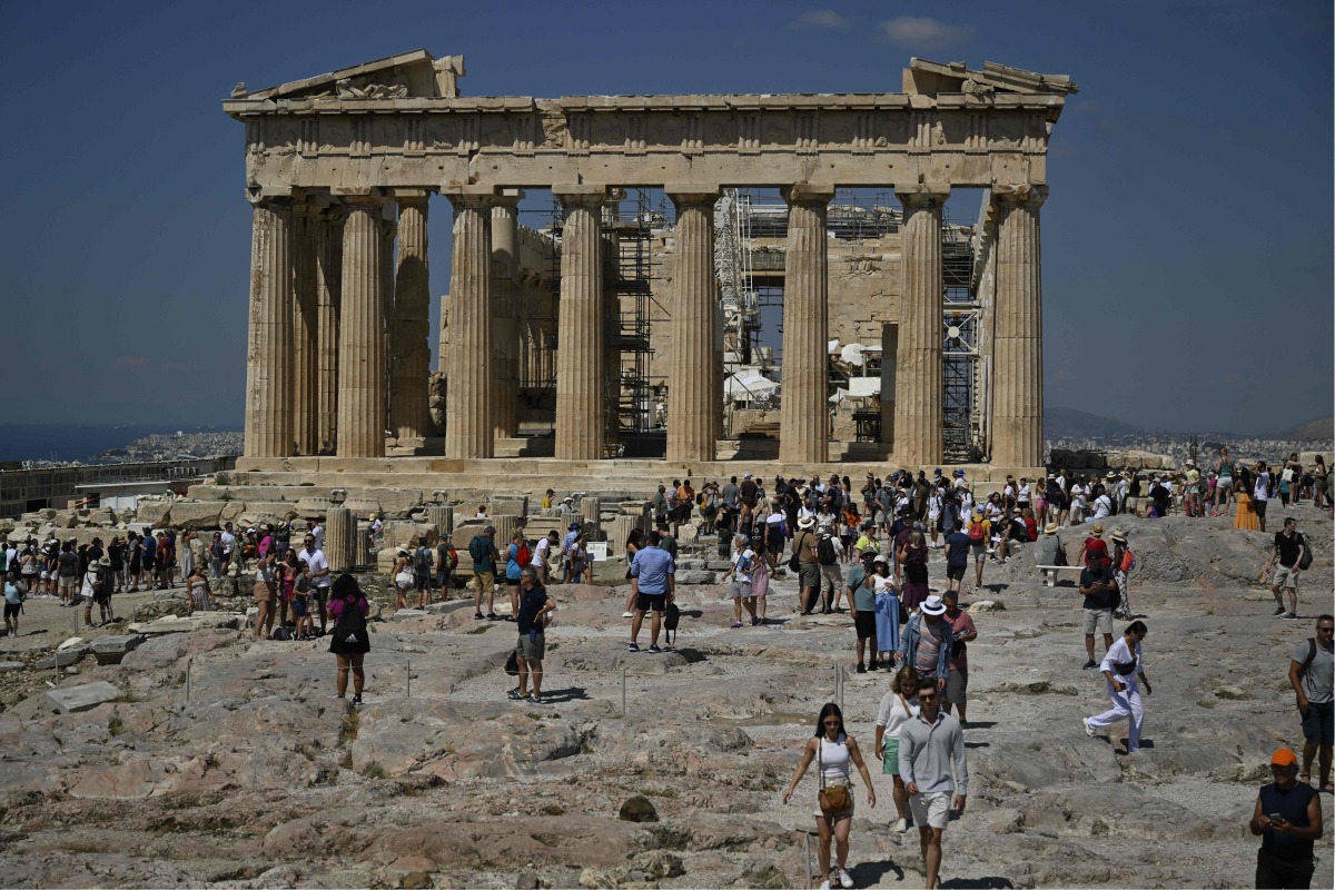 Tourists walk in front of the Parthenon Temple as they visit the Acropolis archaeological site in Athens on June 14, 2023. Photo by Louisa GOULIAMAKI / AFP