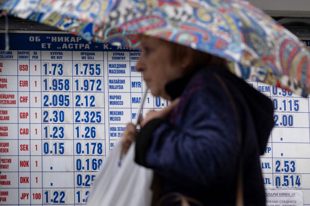 A woman holds an umbrella to protect herself from the rain, as she a walks in front of a currency exchange office in Sofia on May 30, 2025. (Photo by Nikolay Doychinov / AFP)

