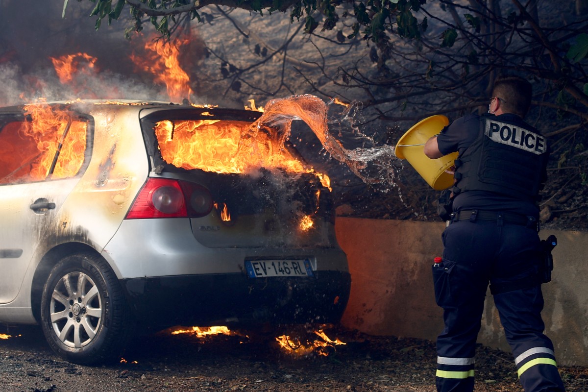 A police officer tries to put off the fire in a car during a wildfire, in L'Estaque district of Marseille, southern France on July 8, 2025. Photo by Clement MAHOUDEAU / AFP.
