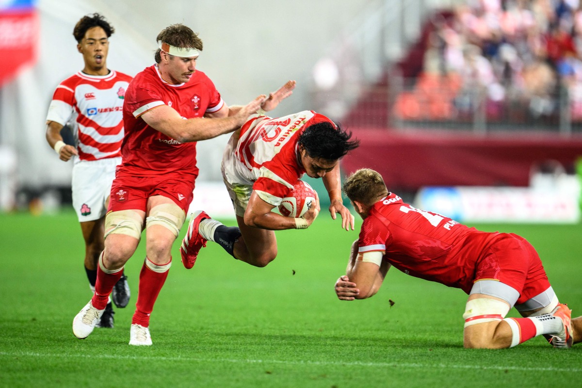 Japan's Shogo Nakano (C) is tackled by Wales' Taine Plumtree (R) during the international rugby union Test match between Japan and Wales at the Noevir Stadium in Kobe on July 12, 2025. (Photo by Philip FONG / AFP)
