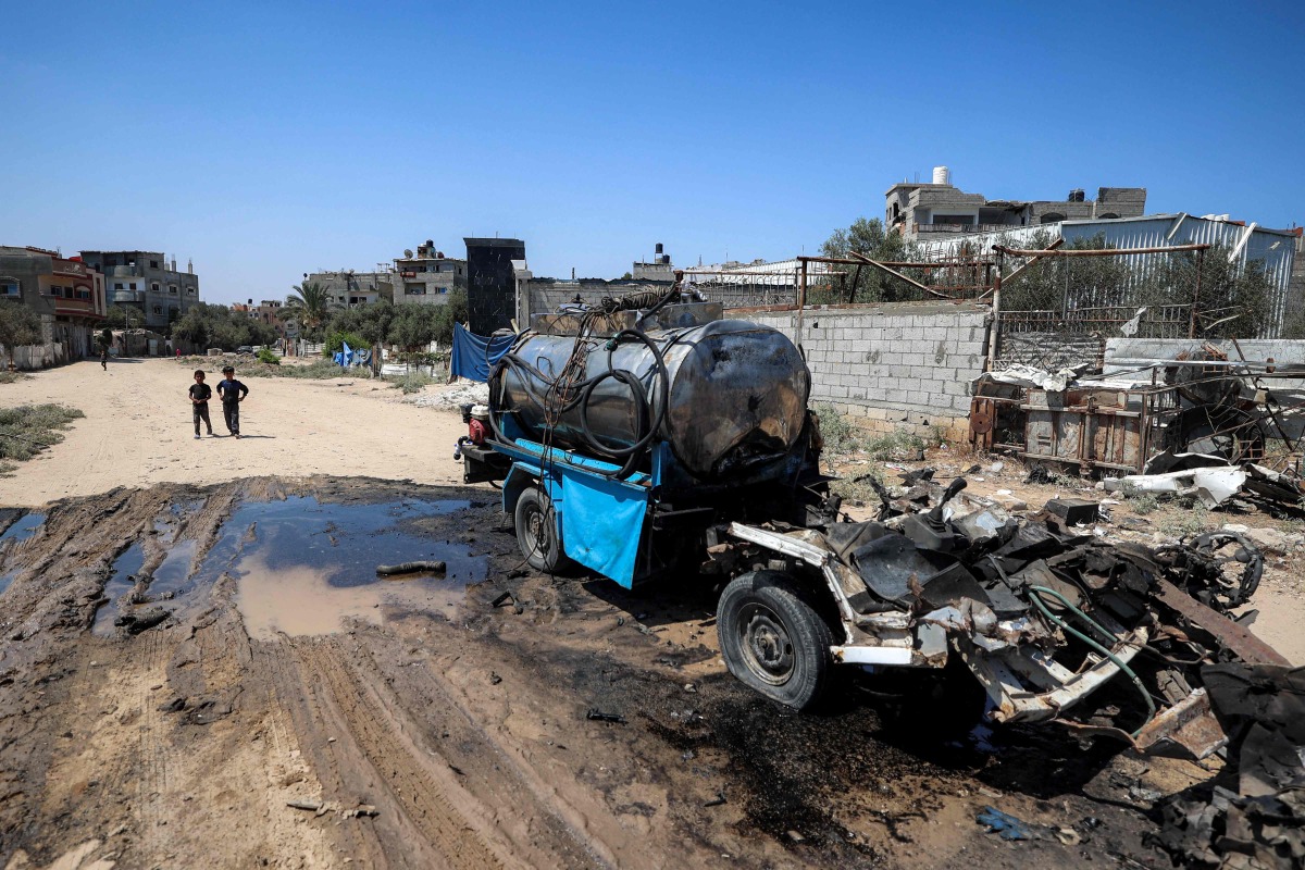 Boys stand near a destroyed mobile water cistern that was hit by Israeli bombardment in the Nuseirat camp for Palestinian refugees in the central Gaza Strip on July 14, 2025. (Photo by Eyad BABA / AFP)
