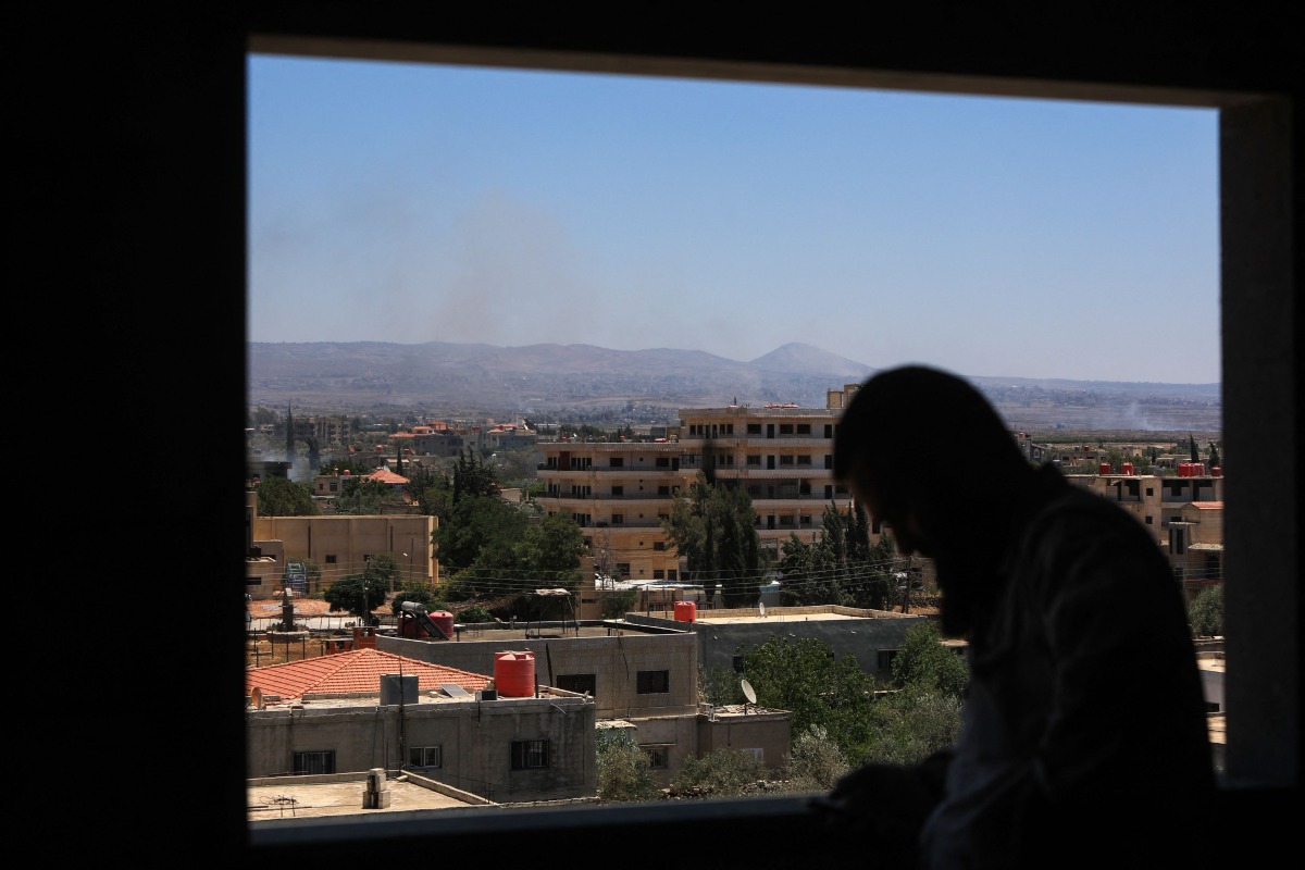 A man stands at a window as smoke billows during Israeli strikes in the vicinity of Syria's southern city of Sweida on July 16, 2025. Photo by Bakr ALKASEM / AFP