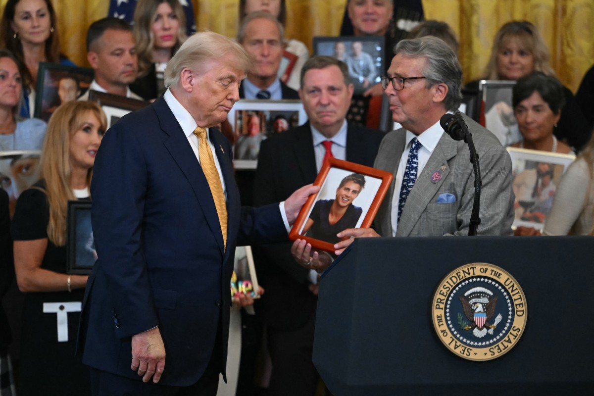 US President Donald Trump (L) looks at a photo as a man who lost his son to fentanyl speaks before the signing of the 