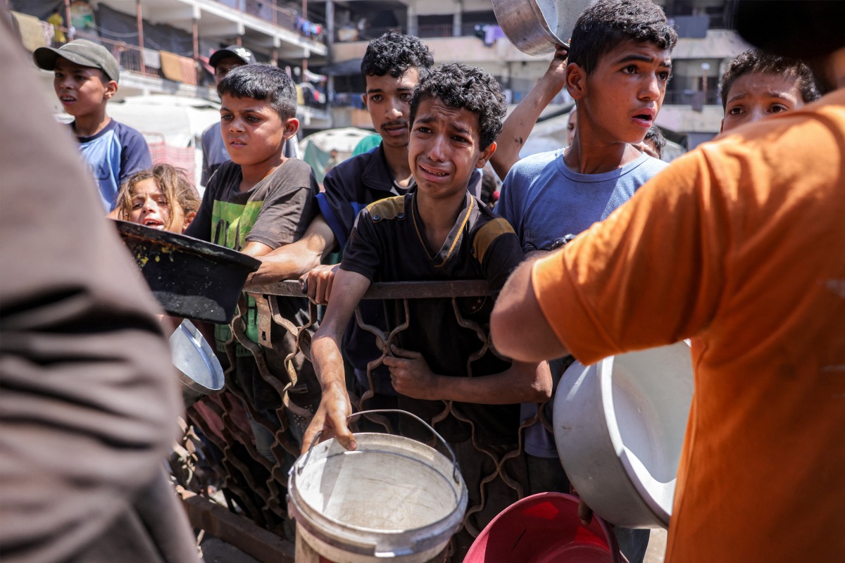 Children queue with pots to receive meals from a charity kitchen in Gaza City on July 14, 2025. Photo by BASHAR TALEB / AFP.
