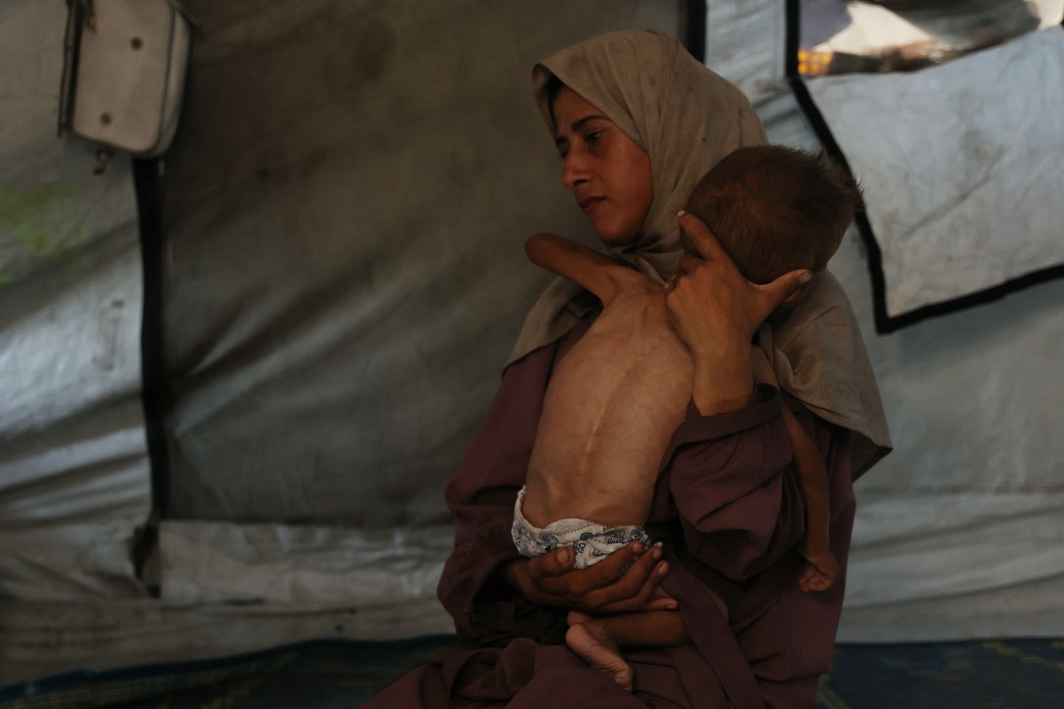 Hidaya, a 31-year-old Palestinian mother, carries her 18-month-old sick son Mohammed al-Mutawaq, who is also displaying signs of malnutrition, inside their tent at the Al-Shati refugee camp, west of Gaza City, on July 24, 2025. Photo by Omar AL-QATTAA / AFP.