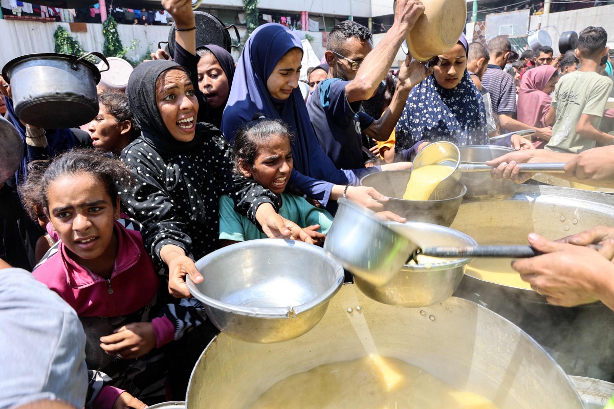 Displaced Palestinians receive lentil soup at a food distribution point in Gaza City in the northern Gaza Strip on July 25, 2025. (Photo by Omar AL-QATTAA / AFP)

