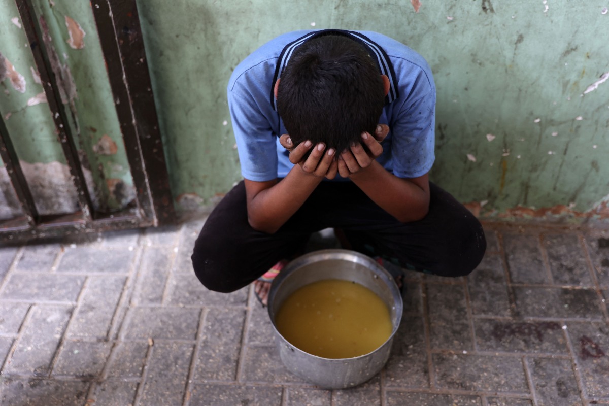 A displaced Palestinian child sits next to a pot of lentil soup that he received at a food distribution point in Gaza City in the northern Gaza Strip on July 25, 2025. (Photo by Omar AL-QATTAA / AFP)

