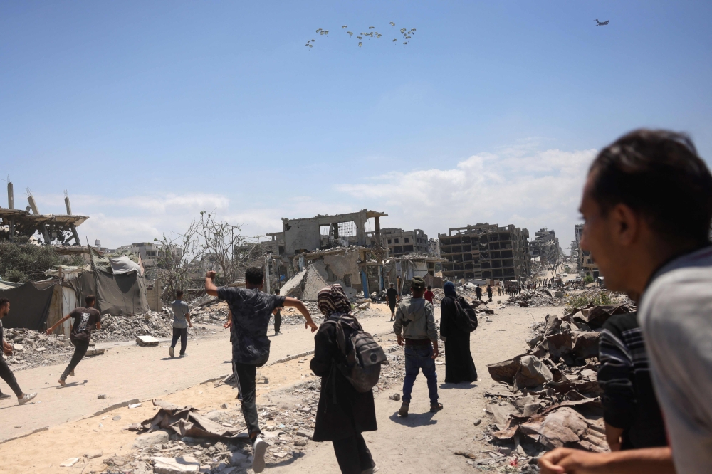 Palestinians in Jabalia in the northern Gaza Strip rush towards a plane conducting an airdrop of aid above the Israel-besieged Palestinian territory on August 1, 2025.  (Photo by Bashar Taleb / AFP)