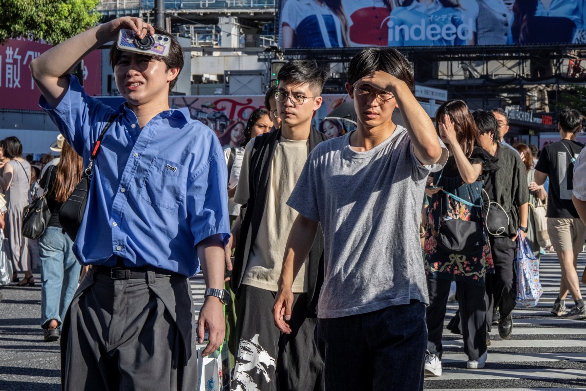 People shield their eyes from the sun as they cross Shibuya crossing on a hot day in Tokyo on July 26, 2025. (Photo by Yuichi YAMAZAKI / AFP)
