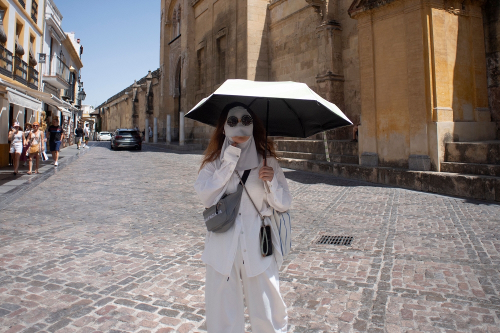 A tourist protects from the sun with a mask and an umbrella during a heatwave in Cordoba, in southern Andalusia region, in Spain, on August 3, 2025. The second heatwave of the year begins on the Iberian Peninsula. (Photo by Jorge Gurrrero / AFP)