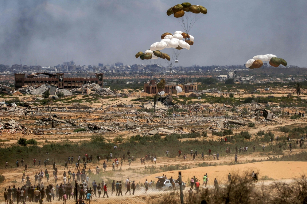 Palestinians rush to the scene as aid pallets are parachuted after being dropped from a military plane over Nuseirat in the central Gaza Strip on August 5, 2025. (Photo by Eyad Baba / AFP)