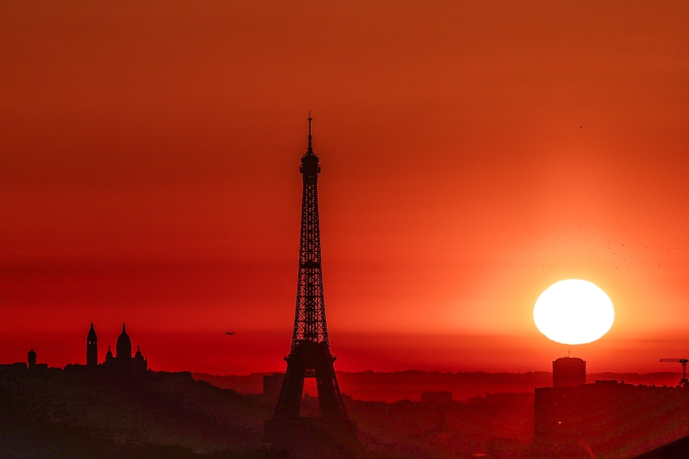 (Files) The sun rises by the Eiffel Tower and the Sacre Coeur Basilica ontop of the Montmartre hill in Paris on July 1, 2025. (Photo by Thibaud Moritz / AFP)