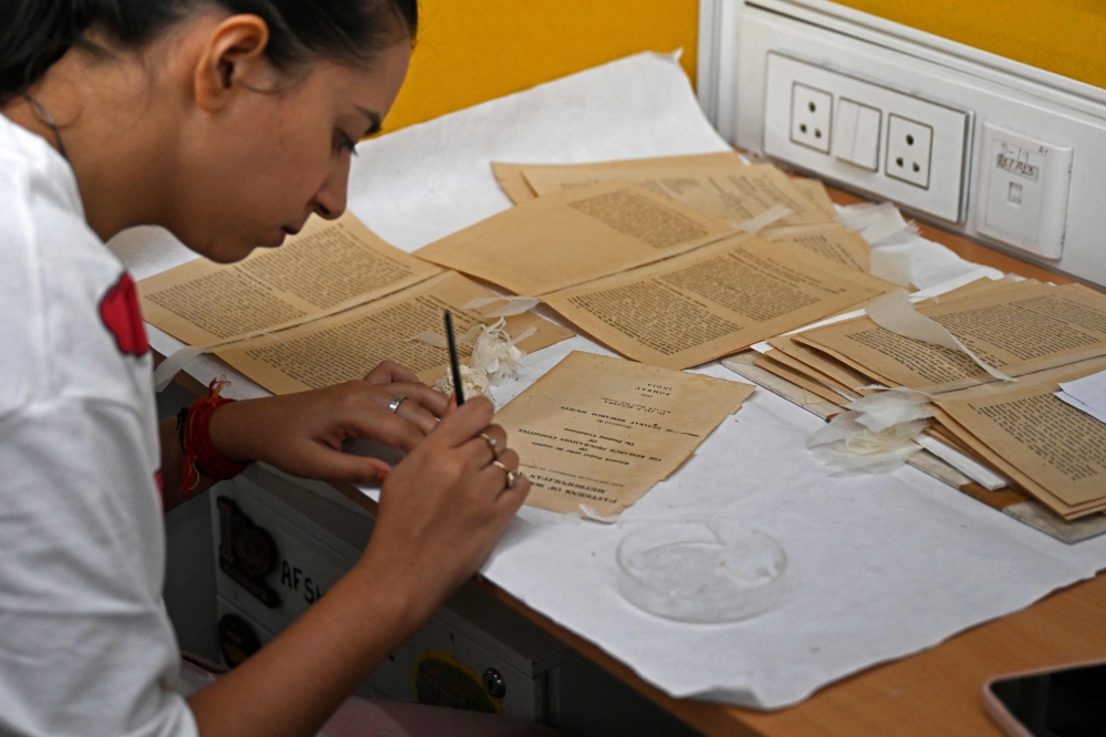 This photograph taken on June 20, 2025 shows an employee working to preserve an old book inside the paper conservation lab of the conservation department at the Indira Gandhi National Centre for Arts (IGNCA), in New Delhi. (Photo by Money Sharma / AFP)