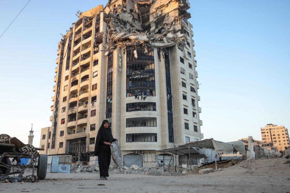 A Palestinian woman walks past a heavily damaged building in Gaza City on August 29, 2025. (Photo by Bashar Taleb / AFP)