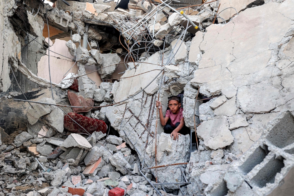 A boy climbs from out of the rubble of a collapsed building that was hit by bombardment in the Nuseirat camp for Palestinian refugees in the central Gaza Strip on August 30, 2025.  (Photo by Eyad Baba / AFP)