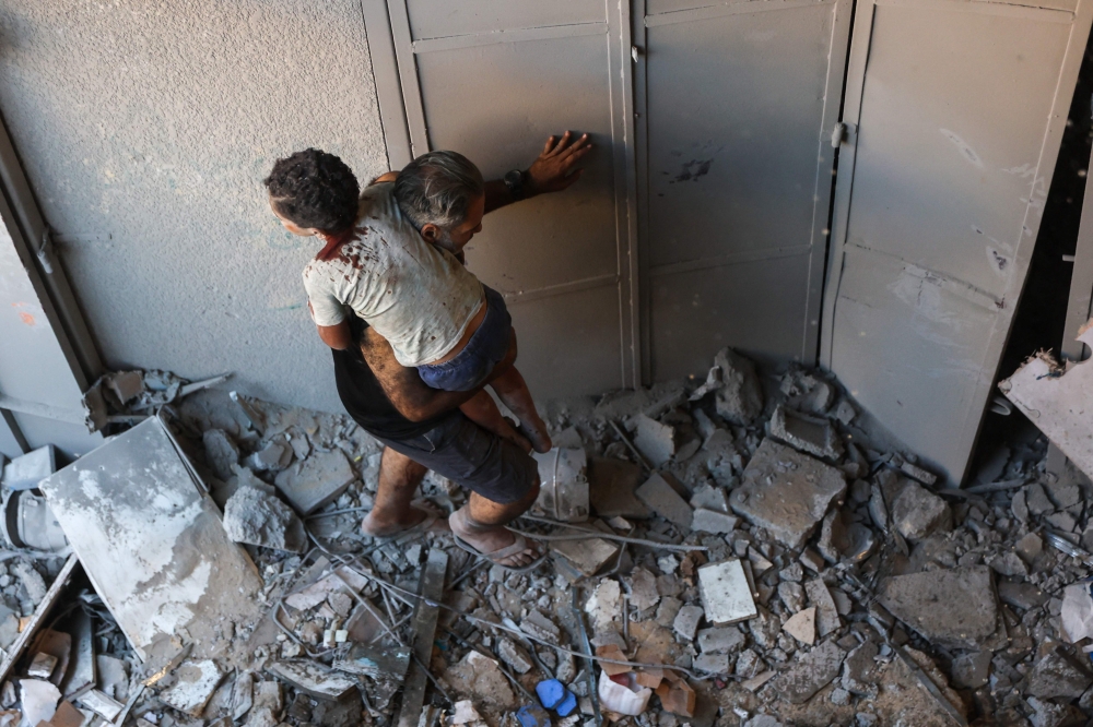 Graphic content / A Palestinian man carries an injured child from inside a building that was targeted in an Israeli strike in the Al-Rimal neighbourhood of Gaza City on August 30, 2025. (Photo by Omar Al-Qattaa / AFP)