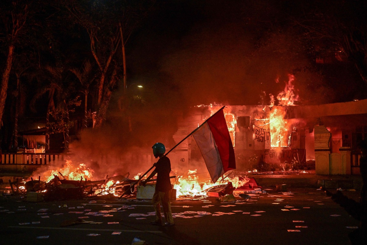 A protester walks with an Indonesian flag in front of a police headquarters that was set on fire and looted during demonstrations in Surabaya on August 31, 2025. Photo by Juni KRISWANTO / AFP