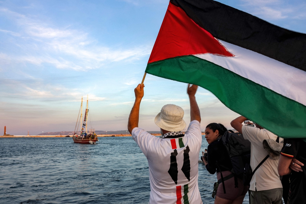 A man waves a Palestinian flags to other activists and human rights defenders riding aboard a vessel departing from Tunisia's northern port of Bizerte on September 14, 2025 to join the last boats taking part in the Global Sumud Flotilla. (Photo by Mohamed Fliss / AFP)
