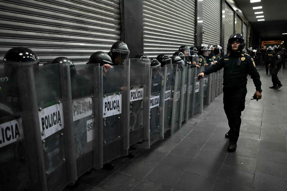Mexican riot police officers take cover behind their shields during a protest over the 11th anniversary of the disappearance of 43 students from Ayotzinapa in Mexico City on September 26, 2025. (Photo by Carl De Souza / AFP)