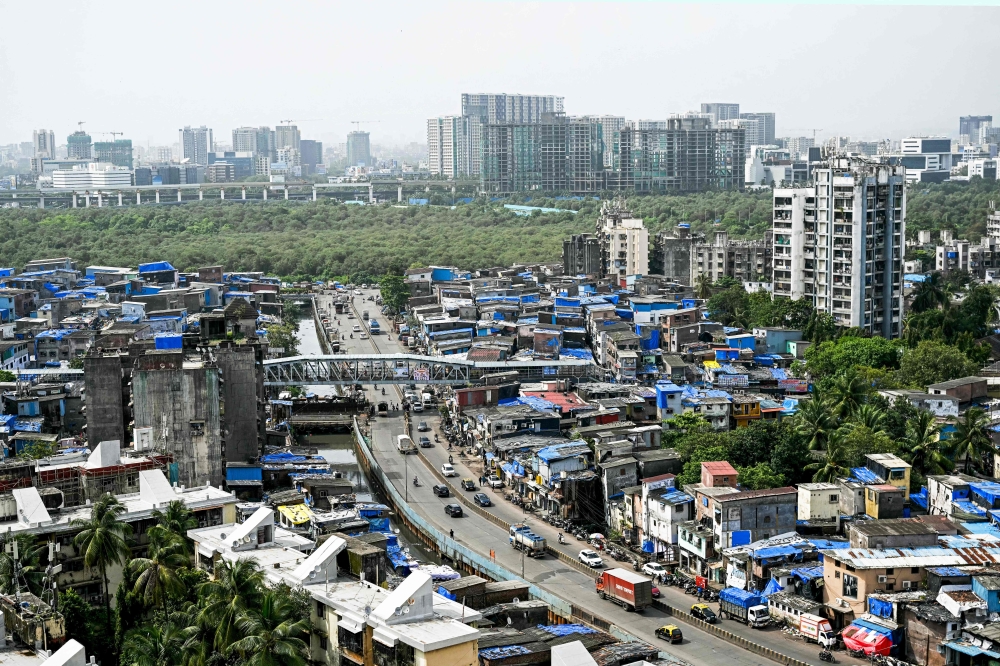 This photograph taken on July 12, 2025 shows high-rise buildings around the cramped shanties of Dharavi, a slum settlement in Mumbai. (Photo by Indranil Mukherjee / AFP)