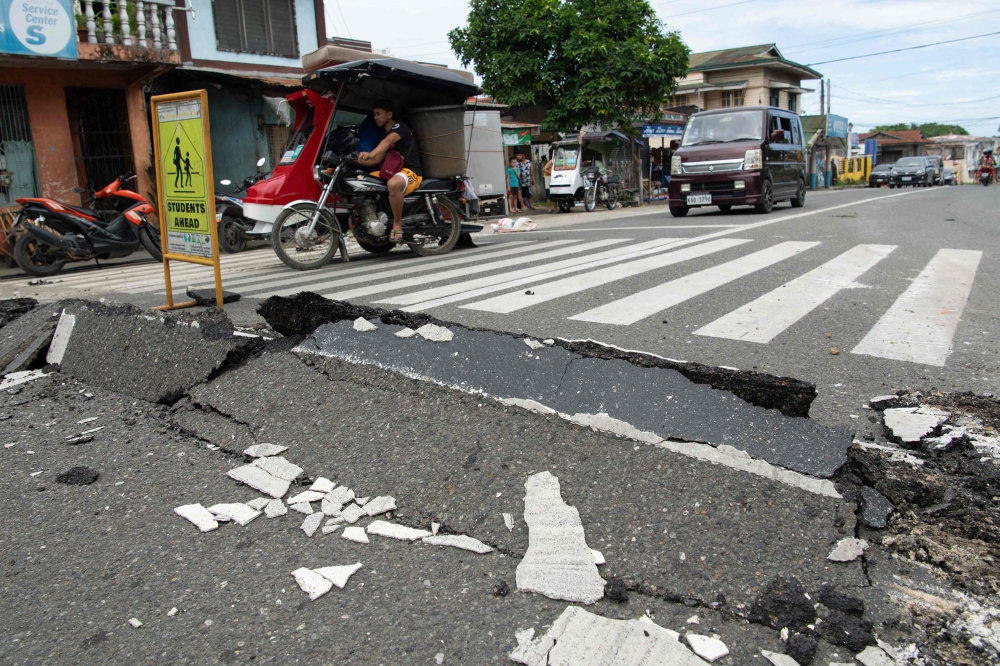 Vehicles maneuver past a damaged part of a road in Bogo City on October 1, 2025, after a powerful 6.9 magnitude earthquake jolted the central Philippines. (Photo by Ted Aljibe / AFP)