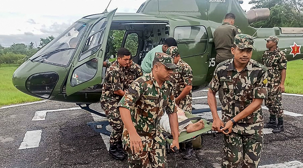 This handout photograph taken and released by Nepal's Army on October 5, 2025 shows Army personnel carrying a landslide victim evacuated by a helicoper following heavy rain-triggered landslides and floods in Nepal. (Photo by Nepalese Army / AFP) 