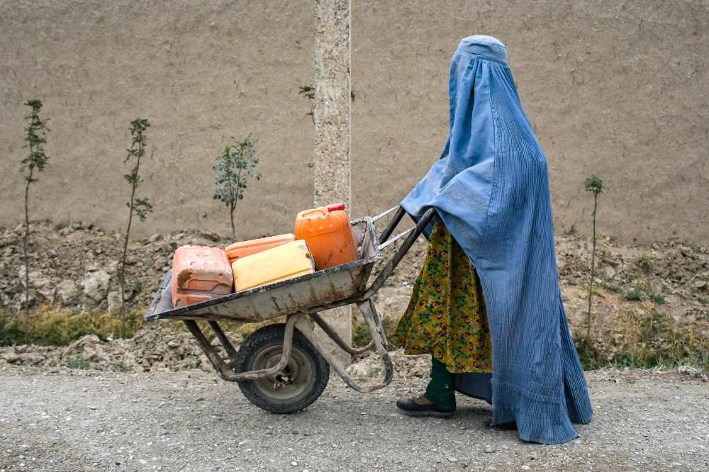 An Afghan burqa-clad woman pushes a wheelbarrow loaded with empty water canisters as she walks along a street in the Koshkak area of the Balkh province on October 5, 2025. (Photo by Atif Aryan / AFP)
