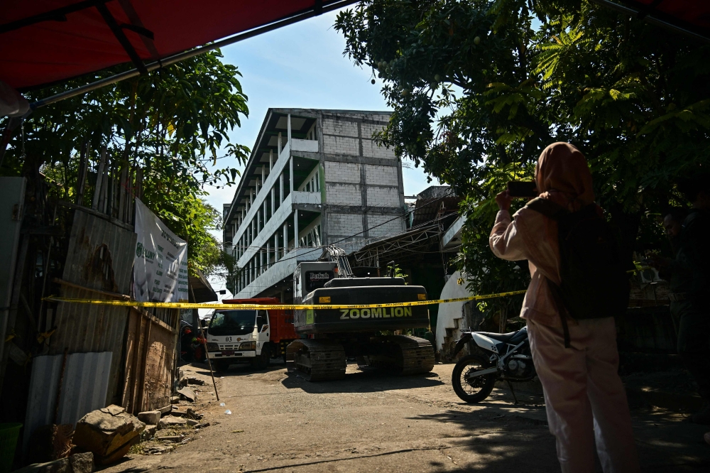 A woman takes a picture in front of the collapsed Al Khoziny Islamic boarding school in Sidoarjo, East Java, on October 6, 2025, as recovery efforts continue. (Photo by Juni Kriswanto / AFP)