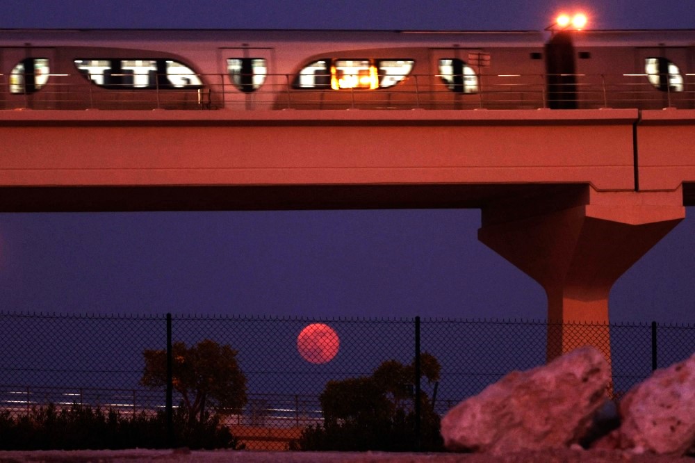 The full moon rises on the horizon as a metro train passes in Doha on October 7, 2025. (Photo by Karim Jaafar / AFP)