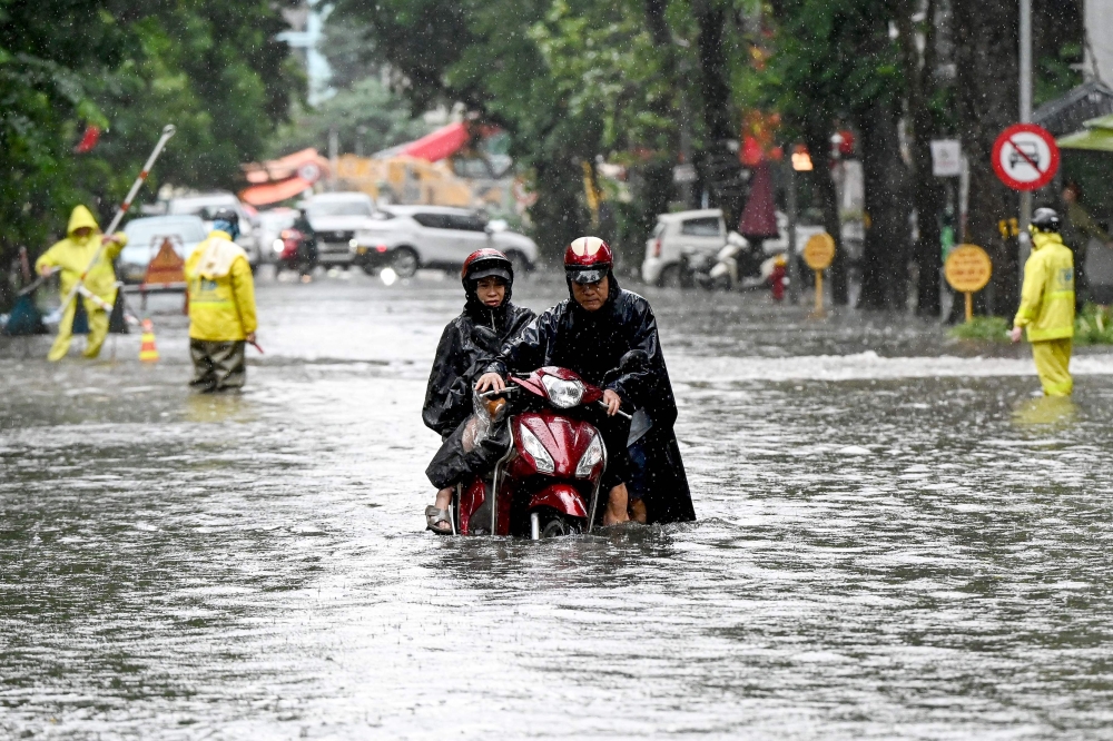 A man pushes his motorbike on a flooded street due to heavy rains caused by Tropical Storm Matmo in Hanoi on October 7, 2025. (Photo by Nhac Nguyen / AFP)
