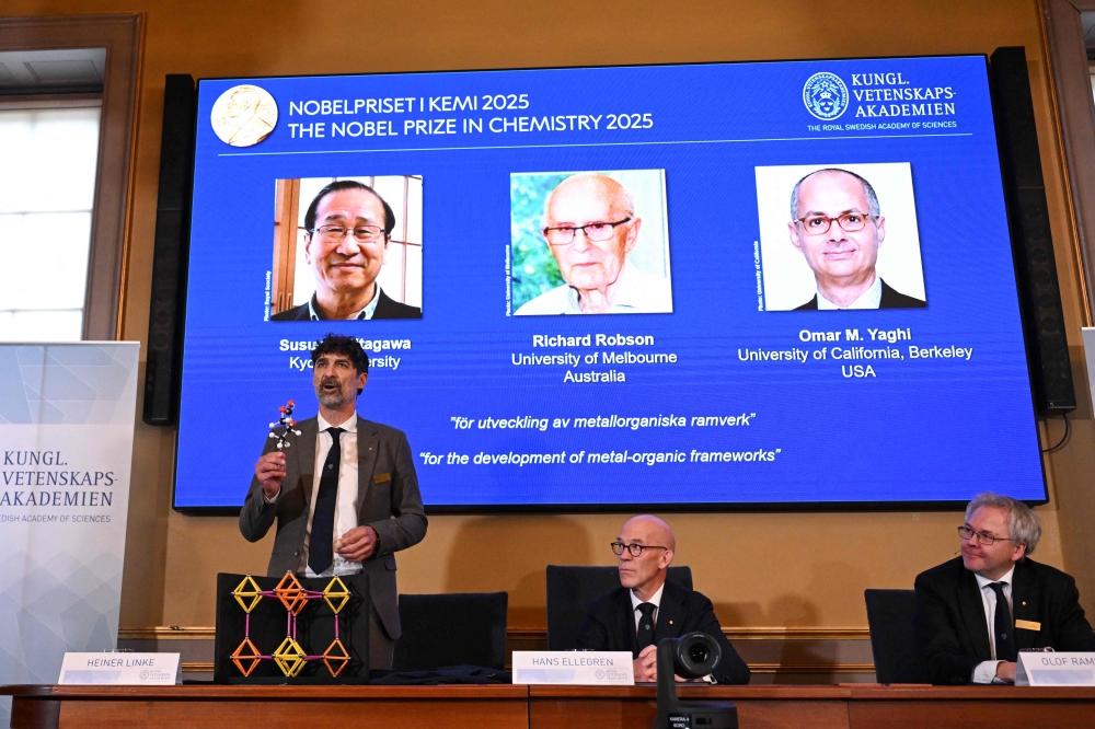 Heiner Linke (L), Chair of the Nobel Committee for Chemistry, explains a model as Hans Ellegren (C), Secretary General of The Royal Swedish Academy of Sciences, and Olof Ramstroem, Member of the Nobel Committe for Chemistry, listen in Stockholm, Sweden, on October 8, 2025. (Photo by Jonathan Nackstrand / AFP)