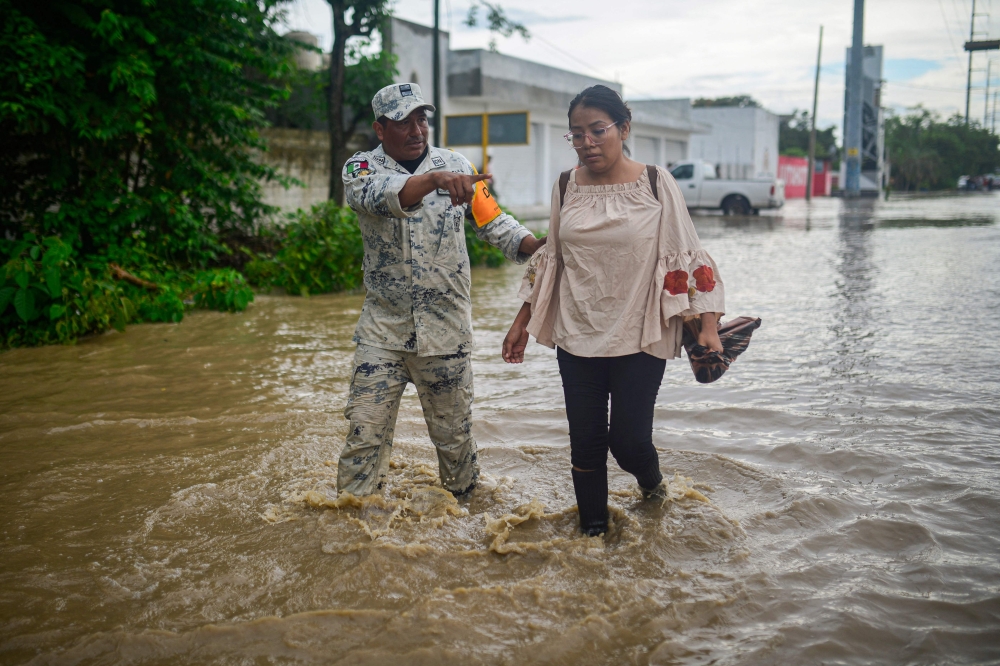 A member of the National Guard helps evacuate a woman through a flooded street following heavy rains in Poza Rica, Veracruz state, Mexico, on October 10, 2025. (Photo by Marco Antonio Perez / AFP)