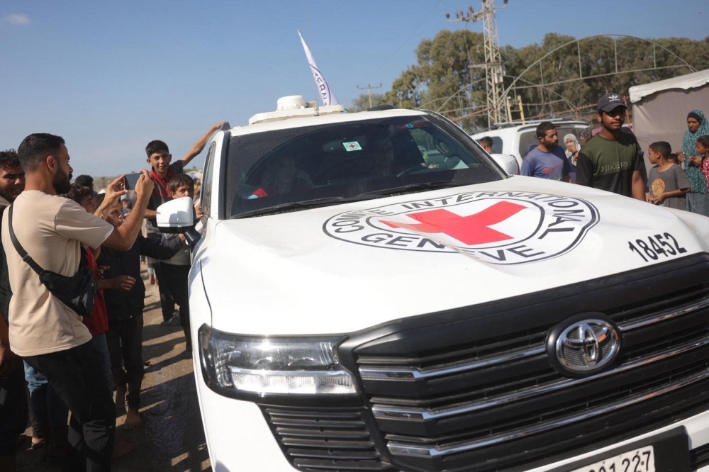 Palestinians gather on both sides of the road as International Red Cross vehicles arrive south of Deir al-Balah in the central Gaza Strip on October 13, 2025. (Photo by Bashar Taleb / AFP)
 